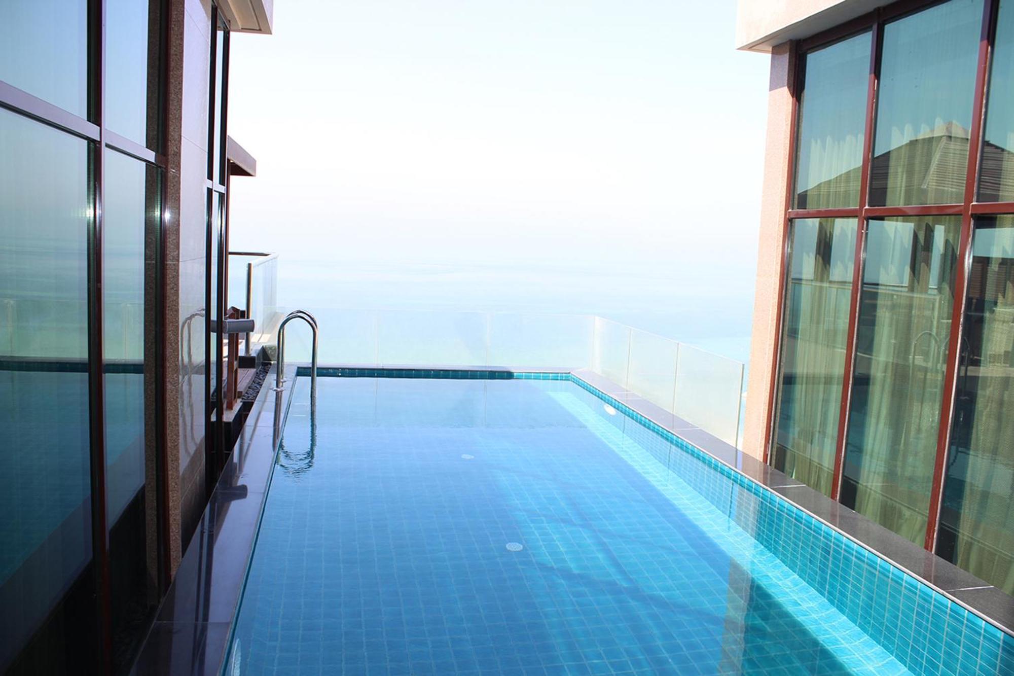Lagoona Beach Luxury Resort And Spa Манама Экстерьер фото The photo shows an infinity pool situated on a balcony or rooftop, with a clear view extending to the horizon. The pool has a sleek design with blue tiles, and it appears to be reflecting the sky. There is a ladder on one side for access into the poo