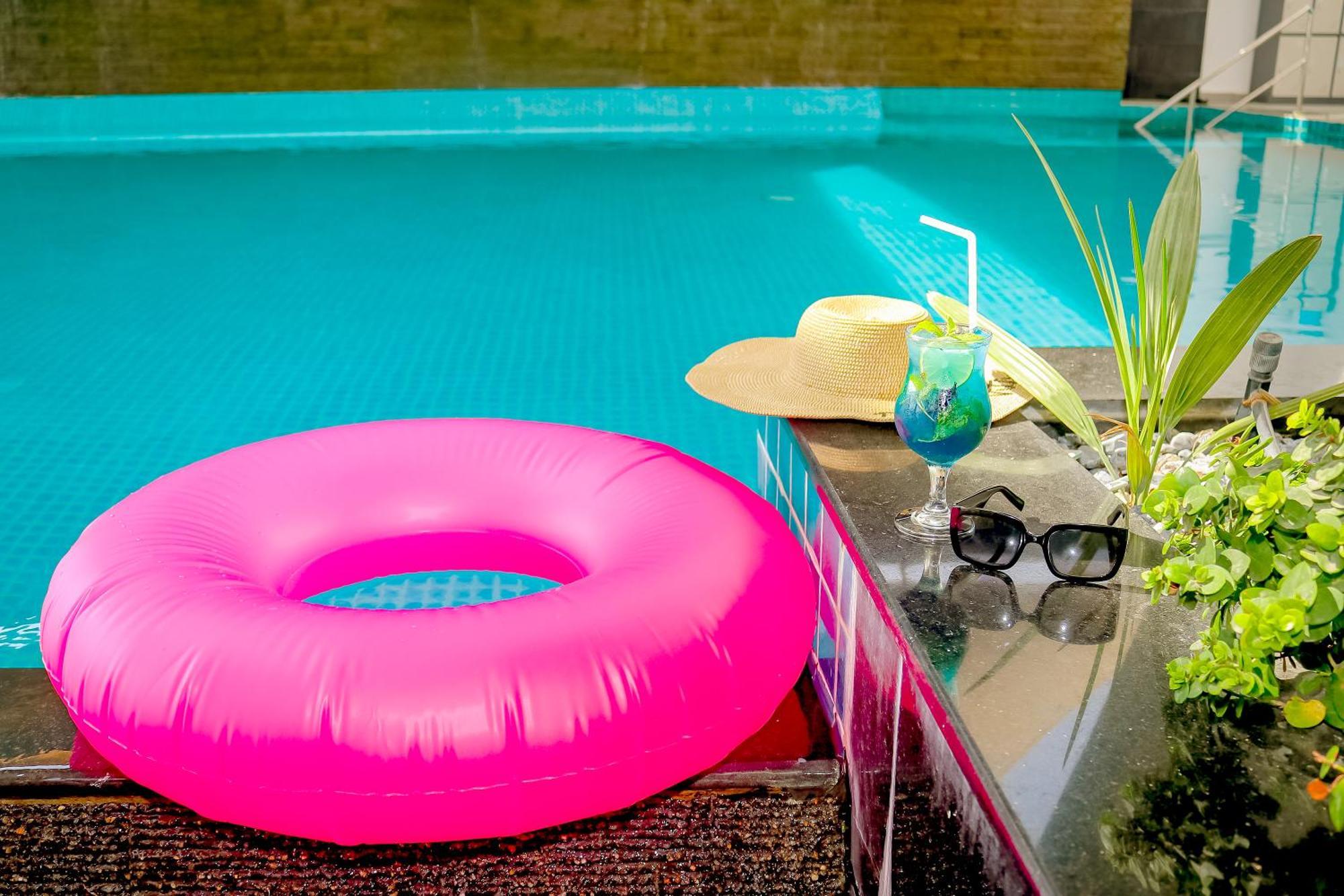 Lagoona Beach Luxury Resort And Spa Манама Экстерьер фото The photo shows a vibrant and inviting scene by a swimming pool. In the foreground, there is a large pink inflatable float and a stylish straw hat. Next to the float, a refreshing cocktail in a glass is displayed, complete with a straw and garnishes.