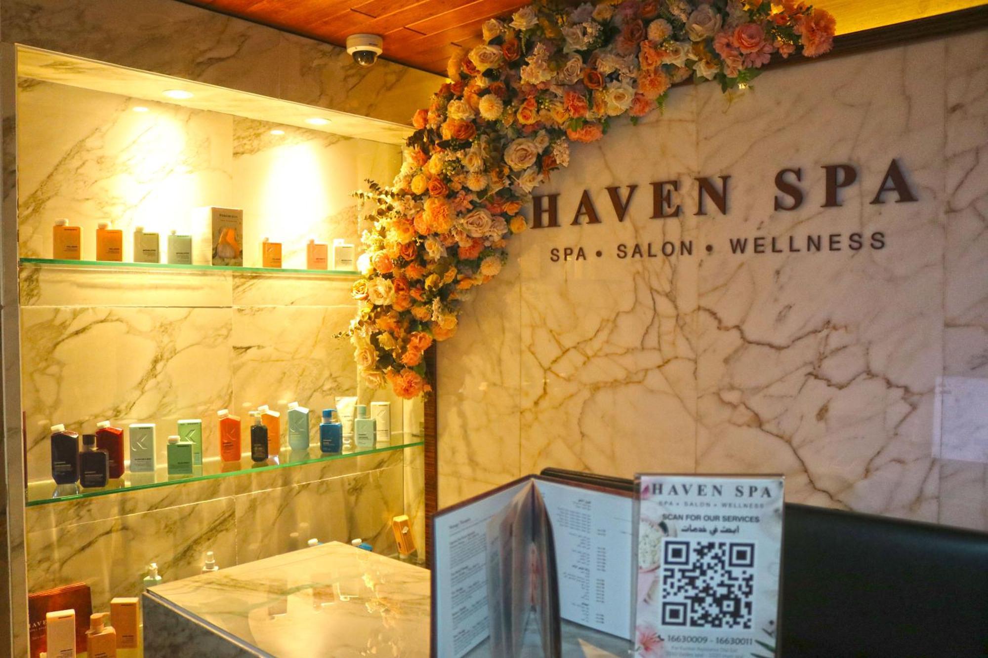 Lagoona Beach Luxury Resort And Spa Манама Экстерьер фото The photo shows the interior of a spa called "Haven Spa." The wall is decorated with beautiful artificial flowers, creating an inviting atmosphere. There are several shelves displaying various colorful bottles and products, likely for skincare or wel