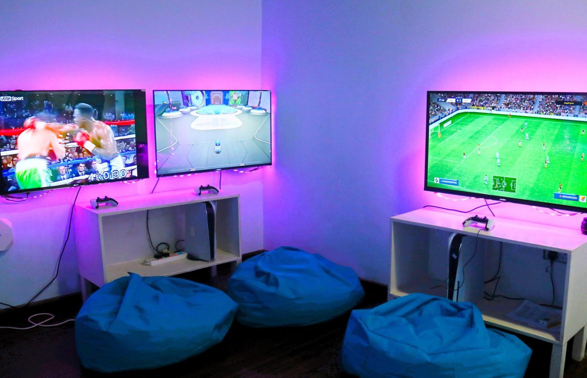 Lagoona Beach Luxury Resort And Spa Манама Экстерьер фото The photo shows a gaming area featuring three televisions mounted on the wall, displaying different games. Two of the TVs are showing gaming scenes, with one depicting a boxing game and the other showing a vibrant game environment. The third TV displ