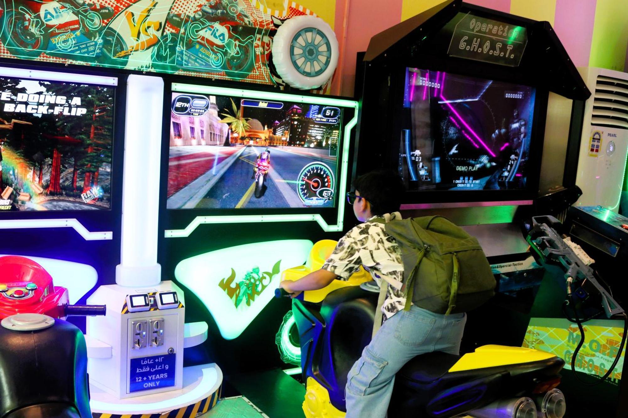 Lagoona Beach Luxury Resort And Spa Манама Экстерьер фото The photo shows a person playing an arcade motorcycle racing game. They are seated on a motorcycle-shaped seat, actively engaging with the game displayed on the screen in front of them. The screen shows a vibrant racing scene with streets and colorfu
