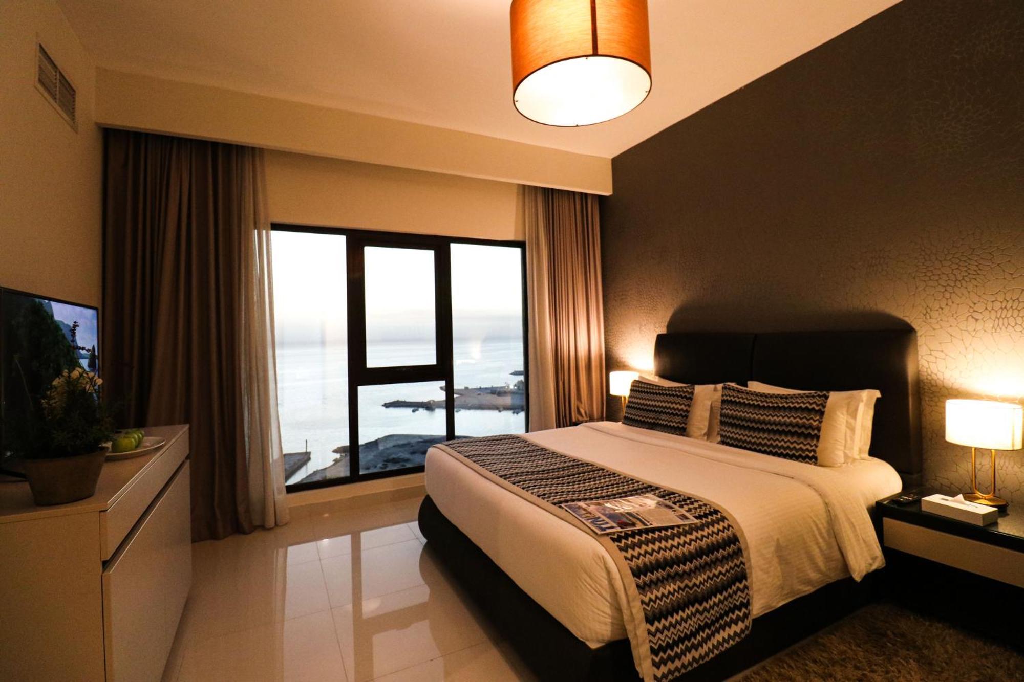 Lagoona Beach Luxury Resort And Spa Манама Экстерьер фото The photo shows a modern hotel room featuring a neatly made bed with decorative pillows. The room has a stylish design with a dark accent wall and a large window that offers a view of the outdoors. Natural light comes in, giving the space a bright an