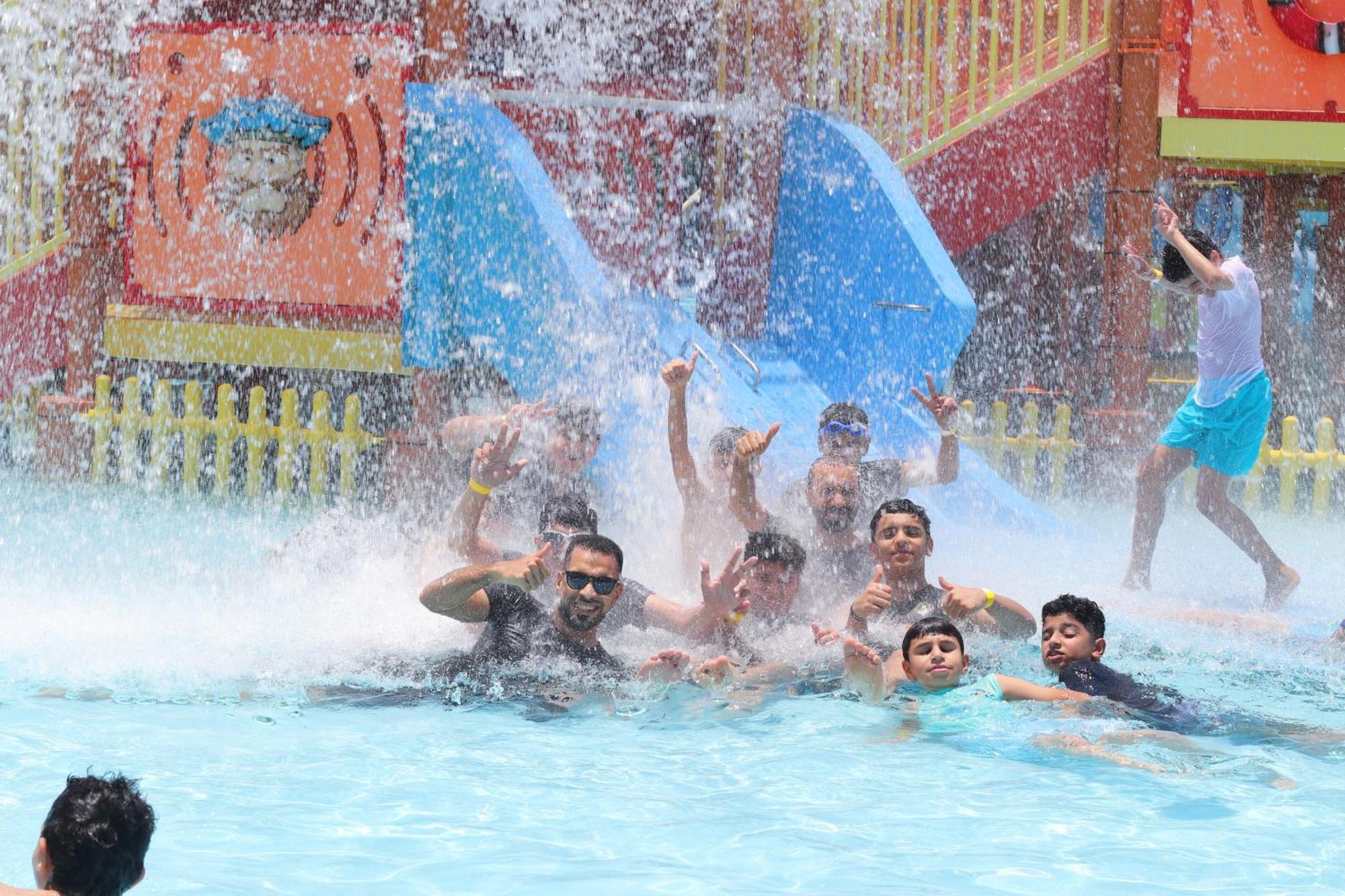 Lagoona Beach Luxury Resort And Spa Манама Экстерьер фото The photo shows a lively scene at a water park or pool area. Several people, including adults and children, are enjoying themselves in the water, splashing and posing for the camera. Water is cascading down, creating a refreshing atmosphere. In the b
