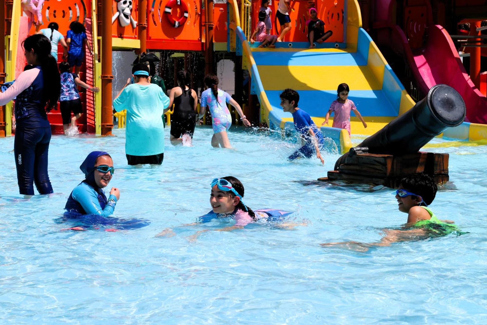 Lagoona Beach Luxury Resort And Spa Манама Экстерьер фото The photo shows a vibrant water park scene with several children playing in a shallow pool. Some are swimming and splashing around, while others are playing on colorful slides in the background. The atmosphere is lively and cheerful, with kids of var