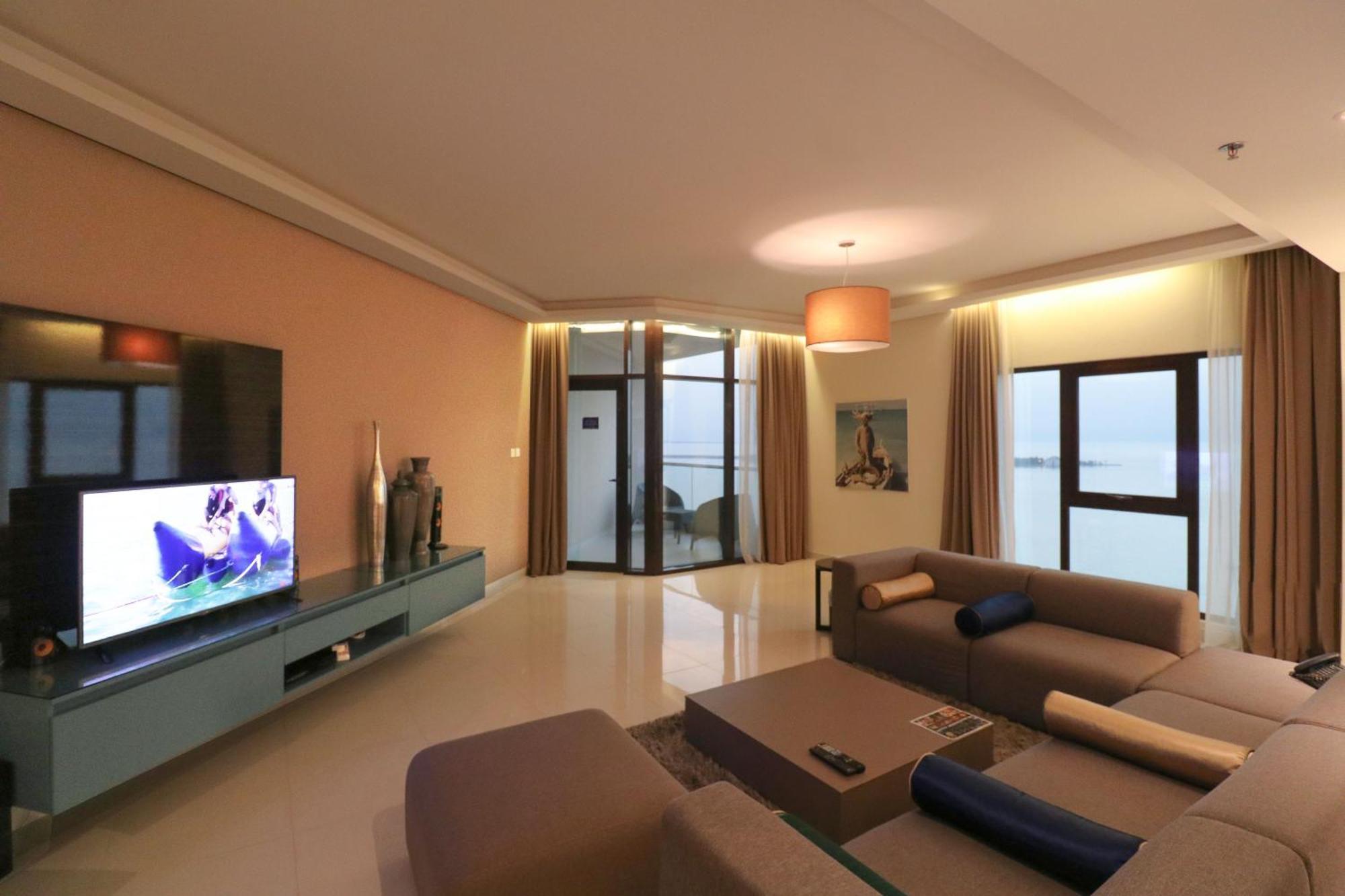 Lagoona Beach Luxury Resort And Spa Манама Экстерьер фото The photo shows a modern living room with a sleek design. There is a large wall-mounted television on a contemporary entertainment unit, with decorative items placed beside it. The room features a comfortable sectional sofa in light tones, with a cof