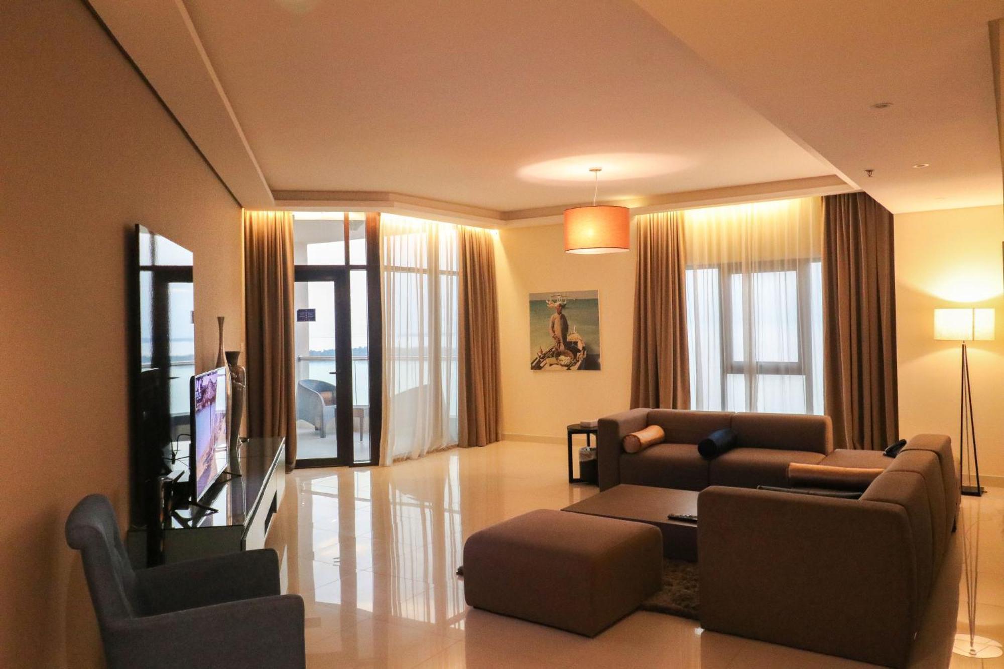 Lagoona Beach Luxury Resort And Spa Манама Экстерьер фото The photo shows a modern living room with a spacious and elegant design. It features a large couch in neutral tones, a soft ottoman, and a stylish coffee table. The walls are painted in a light color, and there are large windows with sheer curtains a