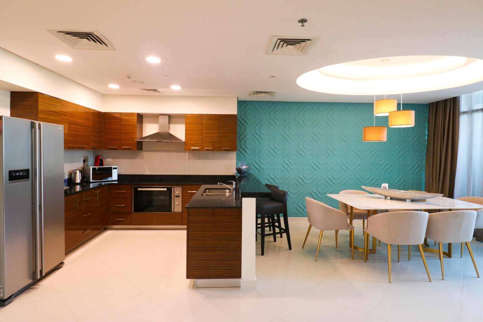 Lagoona Beach Luxury Resort And Spa Манама Экстерьер фото The photo shows a modern kitchen and dining area. The kitchen features wooden cabinets, sleek appliances including a stainless steel refrigerator, microwave, and an oven. There is a dark countertop and a small breakfast bar with high stools. The wall